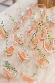 there are many wine glasses with grapefruits and herbs in them on the table