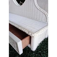 a white wicker bench sitting on top of green grass next to a wall mounted mirror