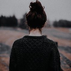 a woman with her back turned to the camera, standing in front of a dirt road