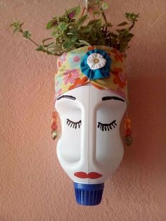 a white mask with flowers on it hanging from the wall next to a potted plant