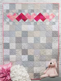 a pink teddy bear sitting next to a quilted wall hanging