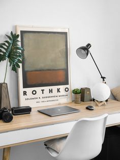 a white desk topped with a laptop computer next to a plant and a poster on the wall