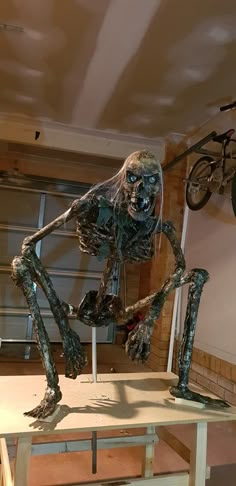 a skeleton sitting on top of a table next to a bike hanging from the ceiling