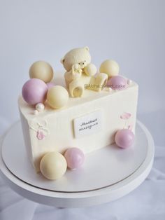 a white cake topped with a teddy bear and lots of balloons