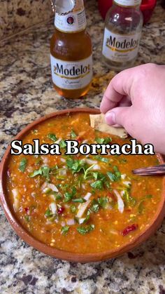 someone is holding a spoon over a bowl of food with salsa borracha in the background