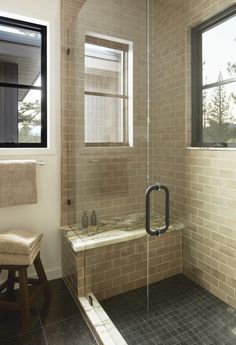 a bathroom with a walk in shower next to a window and a bench on the floor