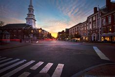 an empty city street with buildings in the background and a church steeple at sunset