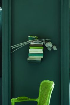 a stack of books sitting on top of a green wall next to a yellow chair