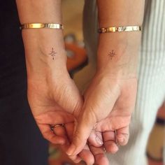 two people holding hands with cross tattoos on their wrist and fingers, both wearing gold bracelets