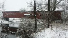 a red covered bridge over a river in the snow