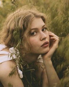 a woman laying in the grass with her hand on her chin and looking at the camera