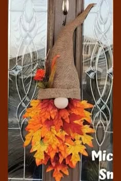 a scarecrow door hanger decorated with fall leaves and a burluck hat