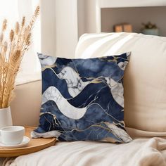 a blue and white pillow sitting on top of a couch next to a cup filled with coffee