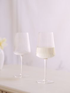 two wine glasses sitting on top of a white table next to a vase filled with flowers