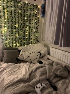 an unmade bed with pillows and remote controls on the bottom, in front of a green curtained window