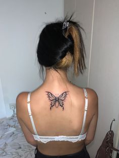 a woman with a butterfly tattoo on her upper back neck and lower back, sitting in front of a bed