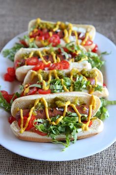 three hotdogs with mustard and ketchup on a white plate next to some lettuce