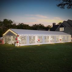 a large white tent with balloons and lights on the grass in front of a house