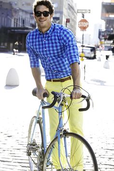 a man in yellow pants and blue shirt standing next to his bike on the street