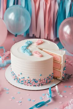 a white cake with blue and pink sprinkles sits on a table next to balloons