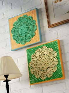 two green and yellow doily art pieces on a white brick wall next to a lamp