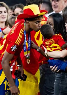 a man in a red shirt and yellow hat is holding a small child while other people look on