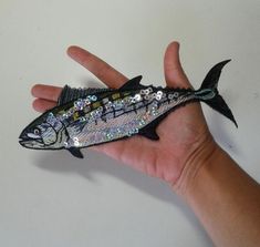 a hand holding a fake fish with sequins on it