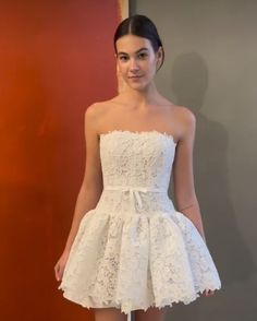 a woman standing in front of a wall wearing a white dress