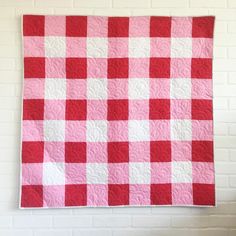 a red and white checkered quilt hanging on a wall next to a brick wall