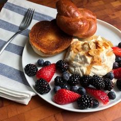 a white plate topped with fruit and pastries next to a bagel on top of a table