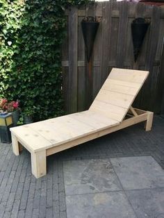 a wooden chaise lounger sitting on top of a brick floor next to a fence