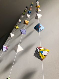 a long line of kites hanging from strings on the side of a white wall