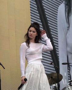 a woman in a white dress is standing on stage with her hands behind her head