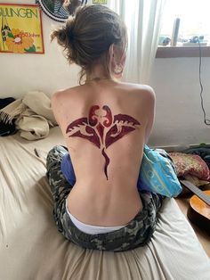 a woman sitting on top of a bed with a tattoo on her back and chest