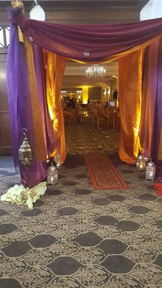 an entrance to a banquet hall decorated with purple and orange drapes, lanterns and flowers