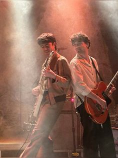 two young men are playing guitars on stage