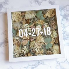 a white box filled with dried flowers on top of a marble counter next to a clock