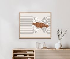 a white vase sitting on top of a wooden cabinet next to a wall mounted art piece