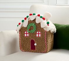 a gingerbread house pillow sitting on top of a white couch next to a green pillow