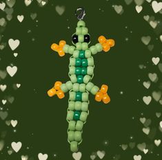 a green and yellow beaded gecko hanging from a string with hearts in the background