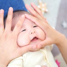 a woman holding a baby in her arms with both hands on top of the baby's face