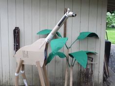 a giraffe made out of cardboard sitting next to a tree with leaves on it