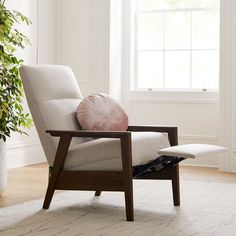 a chair with a pillow on it in front of a potted plant and window