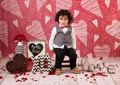 a little boy in a tuxedo and bow tie sitting on a chair next to valentine's day decorations