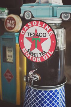 an old fashioned gas station sign on top of a soda dispenser with a car in the background