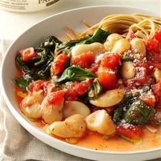 pasta with spinach and tomato sauce in a white bowl next to a bottle of wine