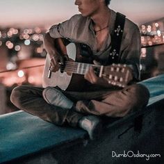 a man sitting on top of a roof playing a guitar