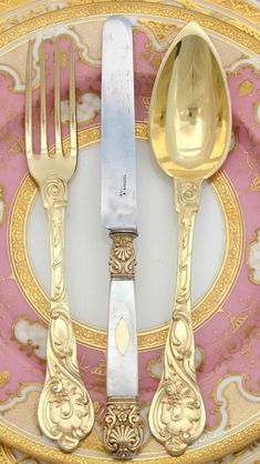 an ornately decorated plate with two forks and spoons on it, in pink and gold