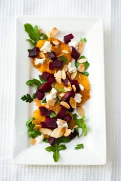 a white plate topped with sliced beets and nuts