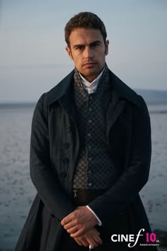 a man standing next to the water wearing a coat and tie